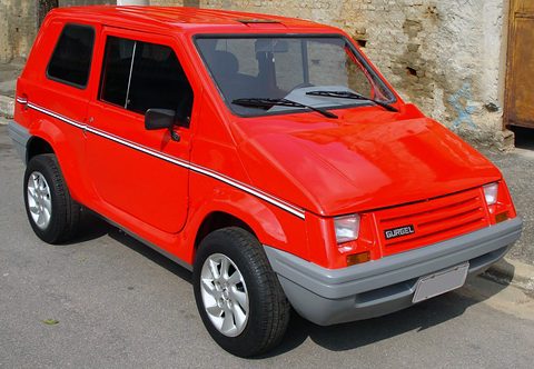 Bright red small two-box car with flat glass, a black grille with the Gurgel badge and grey lower panels, beside an old stone wall. Opens a larger view