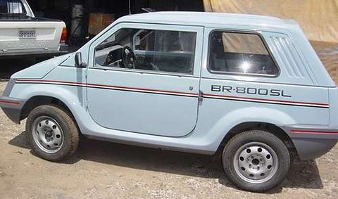 Side view of a pale blue small two-box car with a BR-800 SL script, a louvred rear pillar and a red stripe, on bare ground. Opens a larger view