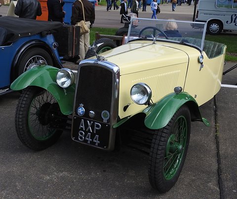 A cream three-wheeler with green wings and wire wheels, an eagle mascot and badges on its radiator. Opens a larger view