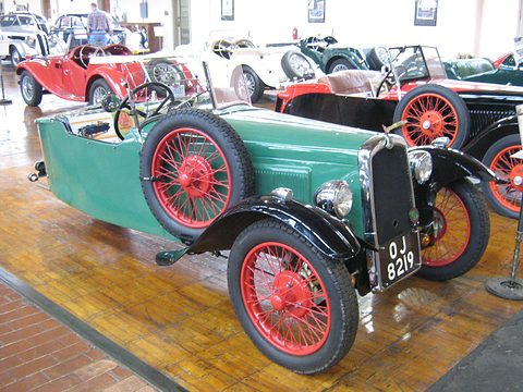 A green sports three-wheeler with black wings, red wire wheels and a spare wheel on its side. Opens a larger view