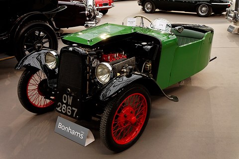 A green three-wheeler with its bonnet raised over a red four-cylinder engine behind a black radiator.