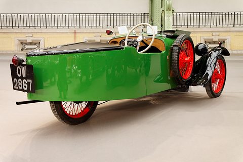 Rear three-quarter view of a long green tapering tail with a number plate, red wire wheels at the front. Opens a larger view