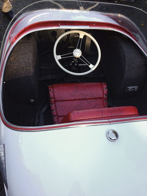Red padded seat and white steering wheel inside a white rounded body, seen from above. Opens a larger view
