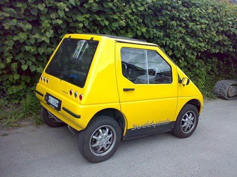 Rear of a yellow rounded microcar with a black lower panel, round tail lamps and buddycab script. Opens a larger view