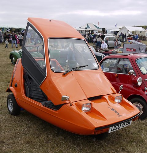 Tangerine three-wheeler on grass with its canopy up and a side screen hanging open. Opens a larger view