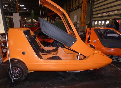 Tangerine three-wheeler side-on with its roof lifted high and a side screen hanging open.