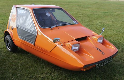 Tangerine wedge three-wheeler with black side screens on a mown field. Opens a larger view