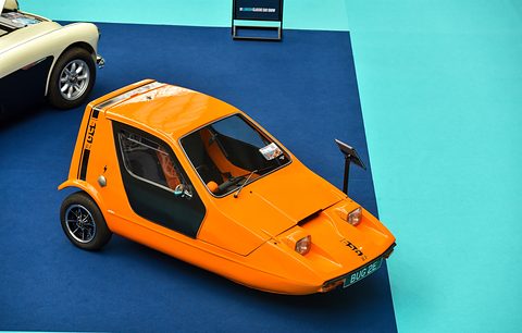 Tangerine three-wheeler seen from above on a blue carpet bordered with turquoise. Opens a larger view