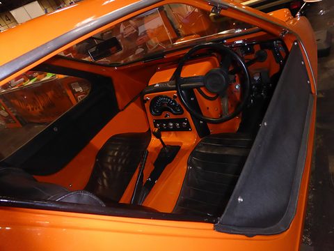 Looking down into an orange cabin: two black seats, a steering wheel and a central engine cover. Opens a larger view