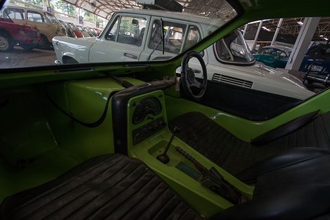 Lime-green interior with black pleated seats, a small steering wheel and the gear lever between them. Opens a larger view
