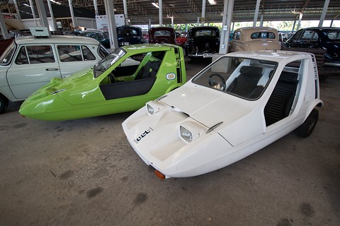 Lime-green and white wedge three-wheelers parked together in a large open-sided museum shed. Opens a larger view