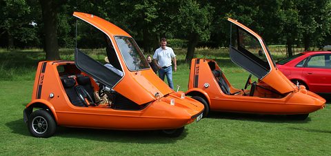 Two tangerine three-wheelers side by side on grass with their one-piece canopies raised. Opens a larger view