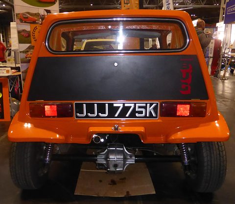Tangerine three-wheeler dead-rear, black tail panel above the rear axle and differential.