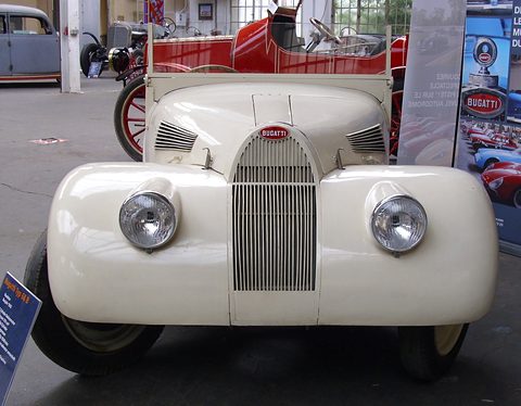 Front view of a cream roadster with a tall slatted horseshoe grille and two round headlamps. Opens a larger view