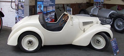 Side view of a small cream open two-seater with rounded wings and a low cut-away door.