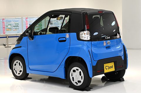 Rear of a bright blue tiny two-seat car with a black tailgate and a C+pod plate on a white floor. Opens a larger view