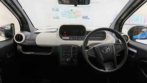White and black dashboard with a centre instrument display, a Toyota steering wheel on the right and round vents.