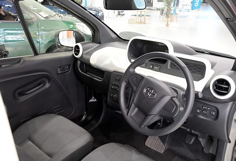Grey seat, a Toyota steering wheel and a white dashboard trim with round vents, seen through the open door. Opens a larger view