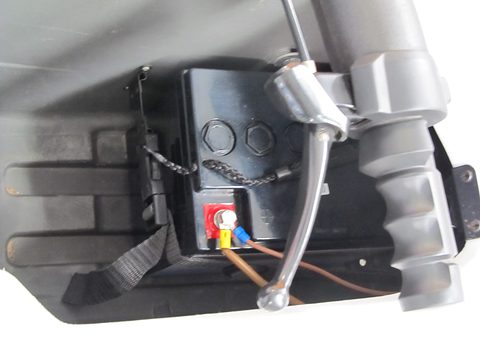 Close view of a black battery with red and blue terminals beside a grey handlebar grip. Opens a larger view