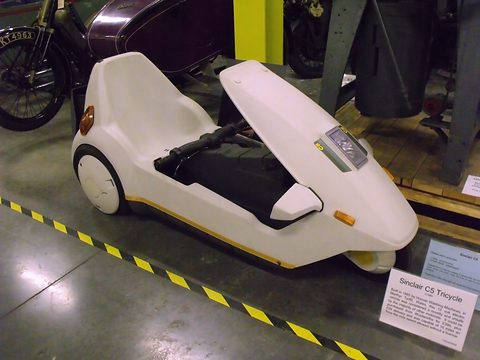 White electric tricycle on a store floor beside hazard tape and an information card. Opens a larger view