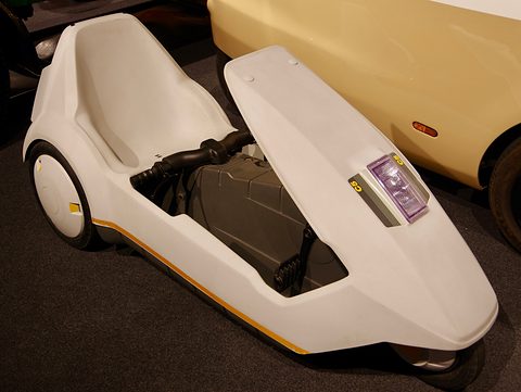 White electric tricycle with its nose lamp and C5 badge, against a dark museum floor. Opens a larger view
