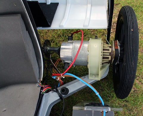 Silver electric motor with coloured wiring mounted beside a narrow rear wheel.