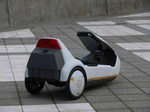 White electric tricycle from behind, a red tail lamp above a dark grey battery housing. Opens a larger view