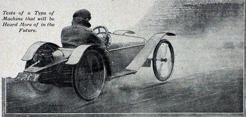 A man in a cap driving a tiny single-seat four-wheeler with its engine behind him, dust streaming from the rear wheels.