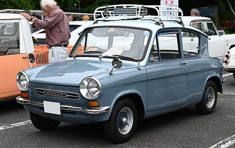 Blue-grey four-door saloon with a white roof rack and chrome bumpers, a man looking at a car behind. Opens a larger view