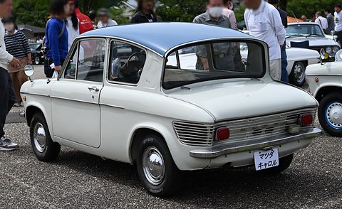 Rear three-quarter of a white saloon with a blue roof and louvred tail, visitors standing behind. Opens a larger view