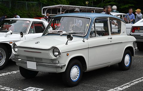 White four-door small saloon with a blue roof and round headlamps, parked among other old cars. Opens a larger view
