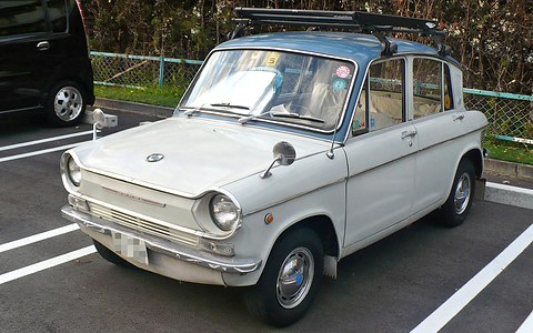 Cream four-door small saloon with a blue-grey roof and a wooden roof rack, in a car park. Opens a larger view