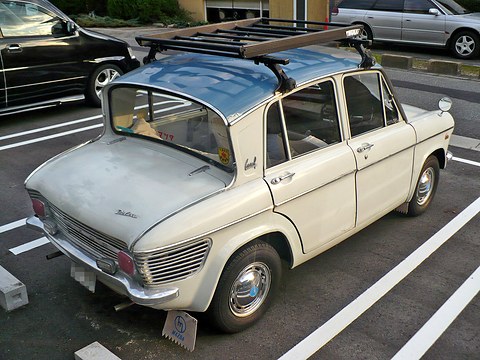Rear three-quarter of a cream four-door saloon with a steeply undercut rear window and louvred tail. Opens a larger view