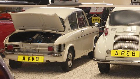 Rear of a white saloon with its lid raised over the engine, a white Subaru 360 parked alongside. Opens a larger view