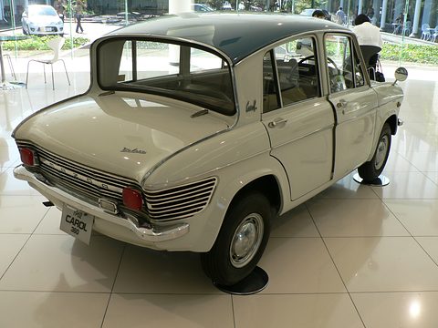 Rear three-quarter of a cream saloon with a steep backward-sloping rear window on a white floor. Opens a larger view