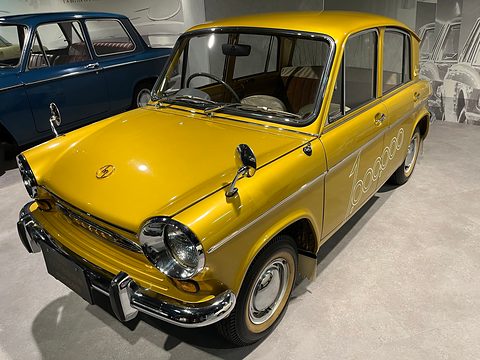 Gold four-door saloon from the front left, chrome bumper and round headlamps, a blue car behind. Opens a larger view