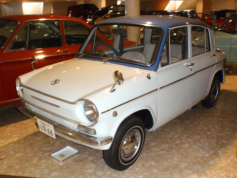 Cream four-door saloon with a blue roof on a beige floor beside a red car. Opens a larger view