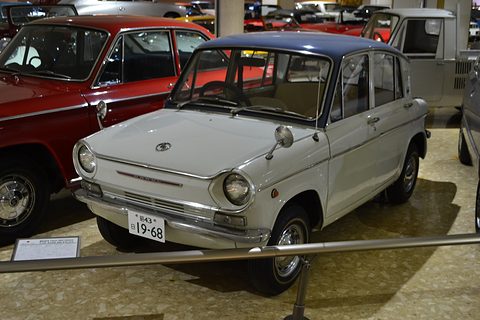Pale grey four-door saloon with a navy roof behind a rail, a red car to its left. Opens a larger view