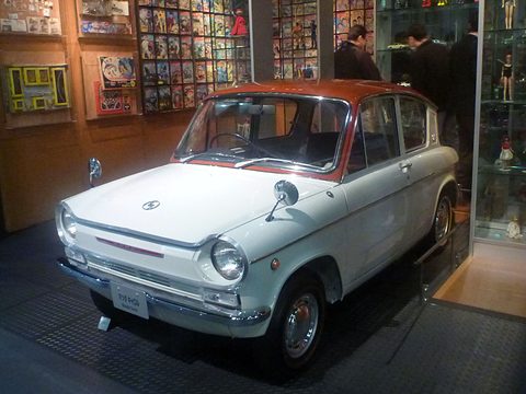 White saloon with a red roof from the front left, shelves of old toys and comics behind. Opens a larger view