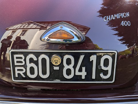 Black plate BR 60-8419 under a chrome lamp, CHAMPION 400 lettering, a house reflected in the paint. Opens a larger view