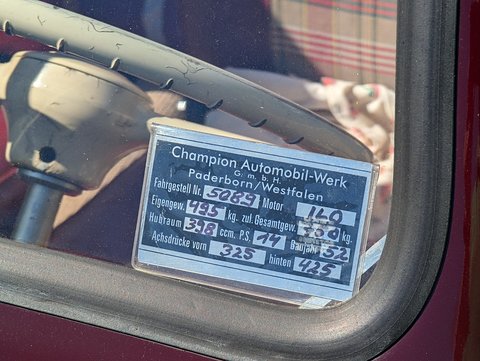 Metal plate reading Champion Automobil-Werk Paderborn/Westfalen with hand-painted figures, behind glass. Opens a larger view