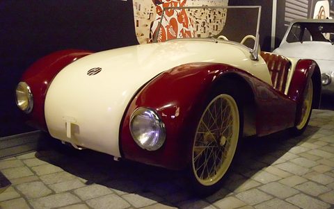 Cream and maroon open two-seater with yellow wire wheels on a cobbled museum floor.