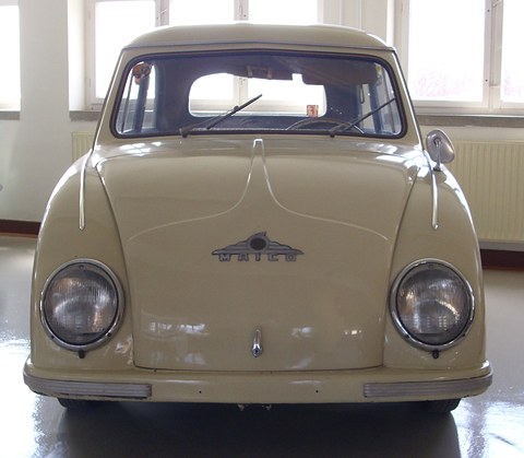 Cream small saloon facing the camera, a winged Maico badge on its bonnet, in a bright hall. Opens a larger view