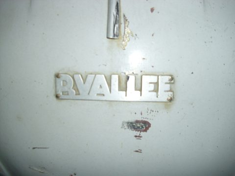 Chrome P. VALLEE nameplate on a pale grey, chipped and scuffed curved body panel.