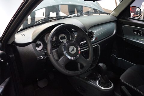 Black and grey dashboard with a three-spoke steering wheel, round dials and a gear selector, seen through the open door.