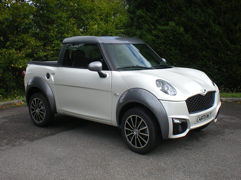 White small pick-up with grey wheel-arch trims and a dark roof, parked on tarmac before a dark hedge. Opens a larger view