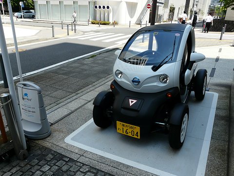 White and black tandem two-seater with a yellow Japanese plate in a marked bay on a city pavement.