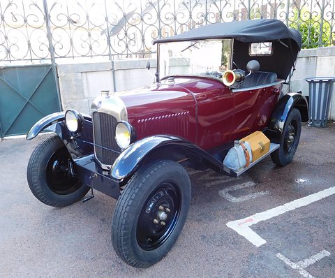A maroon tourer with a black hood and a wooden box on the running board, parked on a marked tarmac lot. Opens a larger view