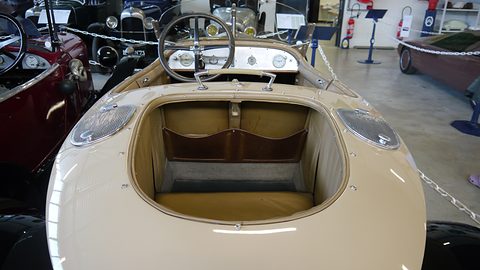 Looking forward over a rounded cream tail into a small cockpit with a steering wheel and leather trim. Opens a larger view