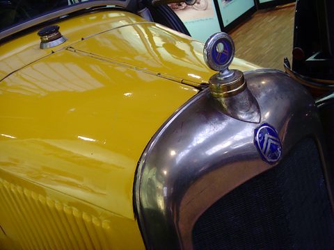A yellow louvred bonnet meeting a nickel radiator shell with a blue chevron badge and motometer. Opens a larger view